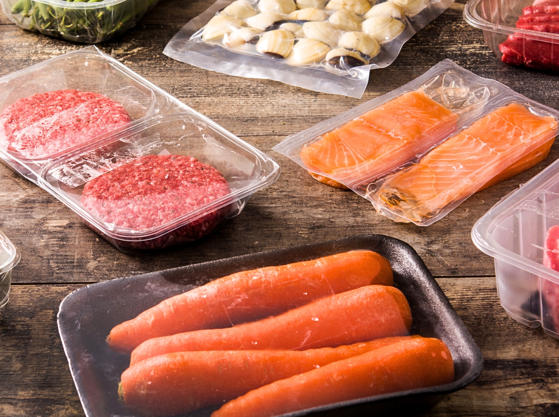 Different types of sustainably packaged food. Meat, green neas, carrots, and salmon on a wooden table.