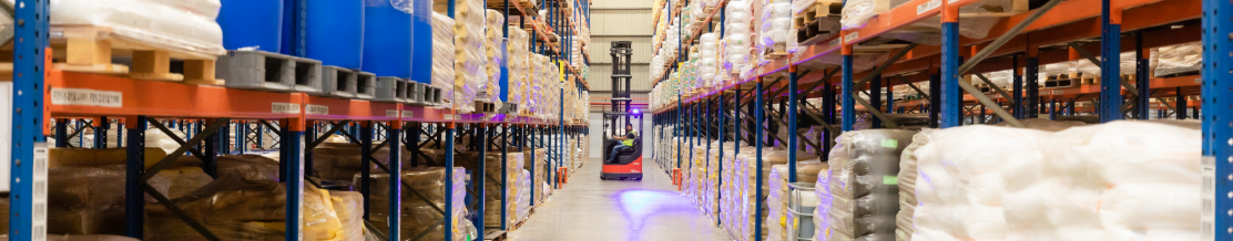 Man driving forklift in the warehouse. Industrial machinery at work in a large warehouse full of chemical goods.