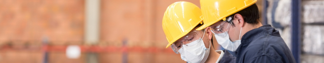 Two safety health environment executive wearing yellow helmet and mask having discussion in a warehouse.