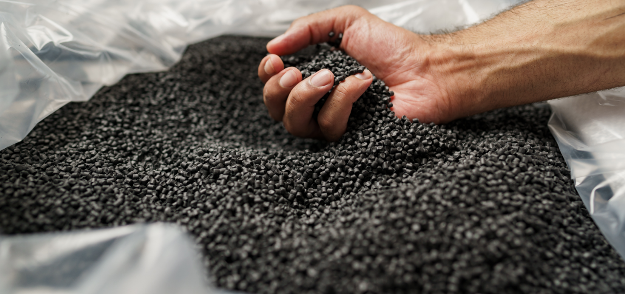 Close up of male hand holding plastic polymer granules. Raw plastics pastilles in black colour.